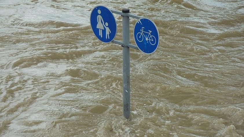 Verkehrsschild für Fußweg und Radweg von Hochwasser umspült.